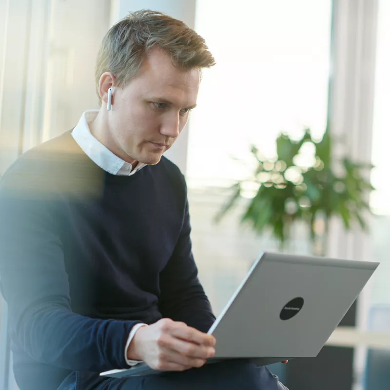 Ein junger Mann mit In-Ear-Kopfhörern arbeitet an seinem Laptop