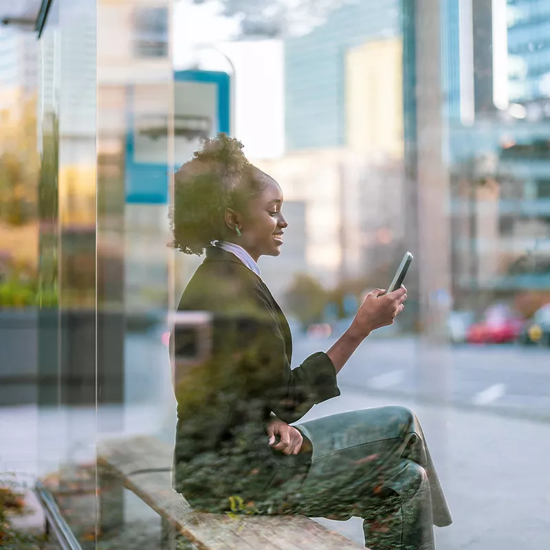 Woman with phone in her hand using Mobility Services sitting on bus station