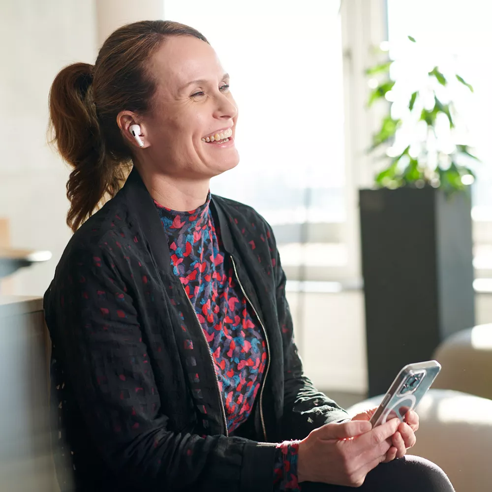 Lächelnde sitzende Frau mit einem Smartphone und In-Ear-Kopfhörern 